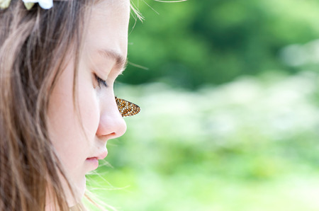 Closeup portrait of boho style surprised girl with butterfly sitting on her nose. Summertime horizontal  outdoors image with slightly vintage filter.の写真素材