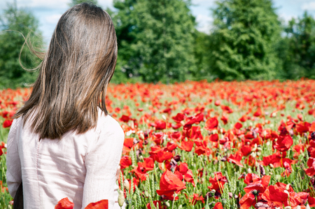 Summer poppy flowers field with girl standing from backside. Outdoors horizontal image with vintage...