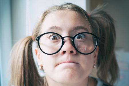 Portrait of glad funny surprised girl with ponytails in glasses. Indoors vibrant closeup horizontal image with filter.