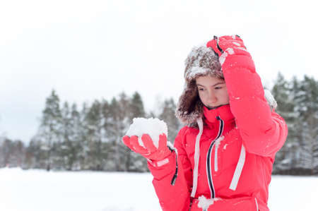 Teenage girl in warm earflap playing with snow in winter forest. Inspirational colored vibrant outdoors horizontal wintertime image.の写真素材