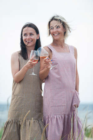 Two young attractive women resting and drinking white wine. Friends/sisters. Summertime outdoors inspirational vertical image with filterの写真素材