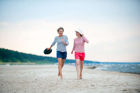 Two young women have fun together on stormy seaside. Friends/sisters. Summertime outdoors inspirational horizontal image. Spectacular cloudy sky backgroundの写真素材
