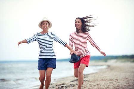 Two young women have fun together on stormy seaside. Friends/sisters. Summertime outdoors inspirational horizontal image. Spectacular cloudy sky backgroundの写真素材