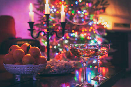 Two champagne glasses on illuminated christmas tree defocused background. Multicolored vibrant...