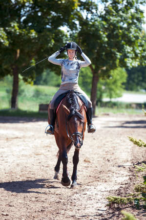 Young pretty at horseback riding training process. Vibrant colored outdoors vertical summertime image with filter.の写真素材