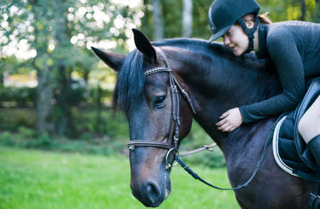 Equestrian lady riding horseback and stroking chestnut horse neck. Vibrant colored outdoors horizontal summertime image with filterの写真素材