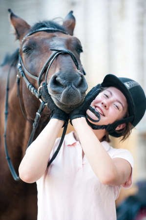 Portrait of funny chestnut horse snout on girl's coach hands. Colored outdoors vertical summertime image with filterの写真素材
