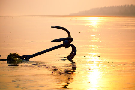 Fishing boat rusty traditional anchor on a beach by the sea.Golden sunlight on sandy beach.の写真素材