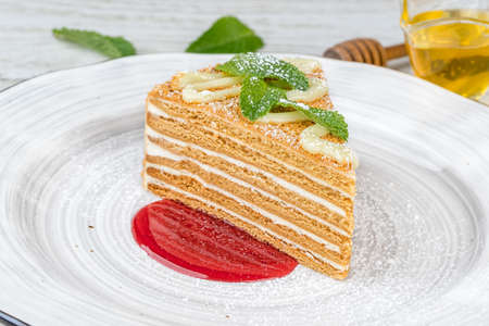 A slice of honey cake on a white plate with jam. Close-up shot