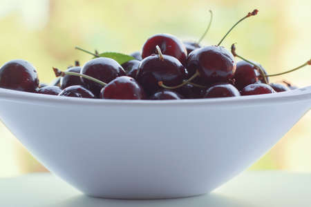 Cherries in white bowl, fruit on outdoor background の写真素材