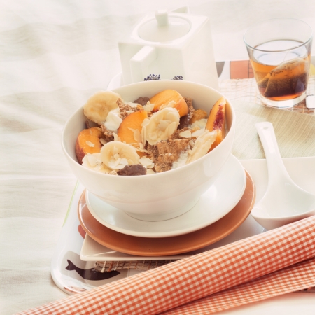 Breakfast in bed tray cereal, peach and banana, yogurt and tea, warm orange color. Square imageの写真素材
