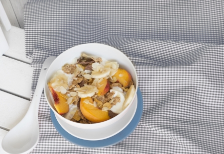 Breakfast in bed tray cereal, peach and banana, yogurt and tea, warm blue color. On white tablecloth and woodの写真素材