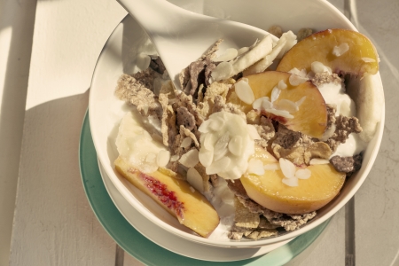 Breakfast in the sun, cereal bowl, peach and banana, yogurt on blue plate and warm vintage  color. White on woodの写真素材