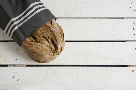 rustic bread, wrapped in striped fabric on white wooden background