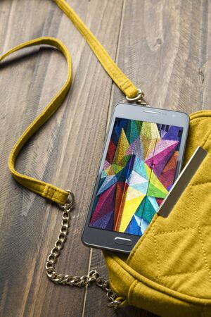 Mobile phone and yellow handbag women ond wood backgroundの写真素材