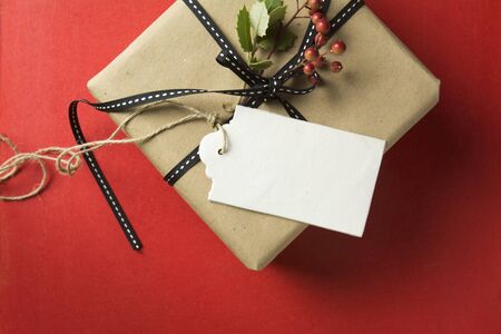 Christmas Gift box, wrapped in recycled paper, black bow with empty tag on red background