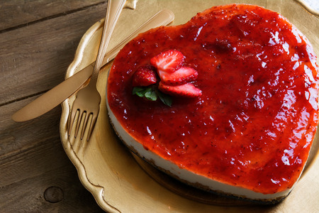 Heart shaped cheesecake with raspberry jelly on a gold plate decorated with strawberriesの写真素材
