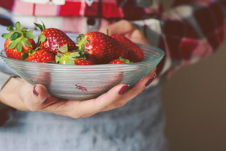 bowl of strawberries in the hands of a woman with apronの写真素材