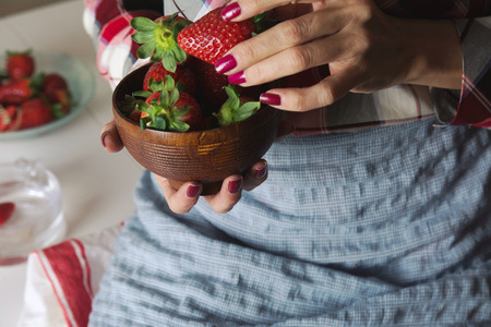 bowl of strawberries in the hands of a woman with apron, sitting at the tableの写真素材