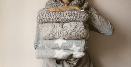 Woman holds a stack of woolen clothes, folded, winter sweaters, gray.の写真素材