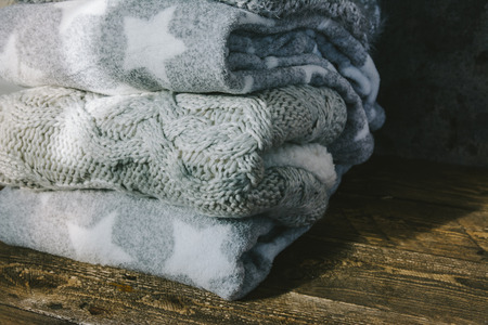 Pile of knitted winter clothes on wooden background, sweaters, knitwear, in a rustic setting.