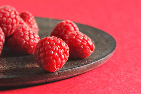 Fresh raspberries on rustic black plate, red background