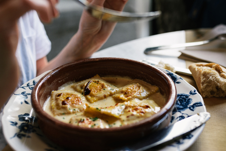 Person eating ravioli with gratin cheese, on the antique plate in restaurant