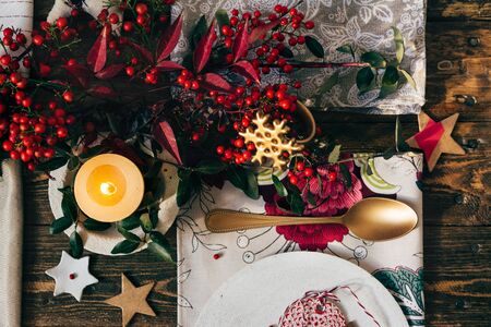 Candle lit on the Christmas table, surrounded by festive decoration, on the place setting