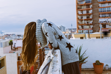 Woman on the roof terrace, looking down, with the hair falling in the vacuum, with the views of the city in the backgroundの写真素材