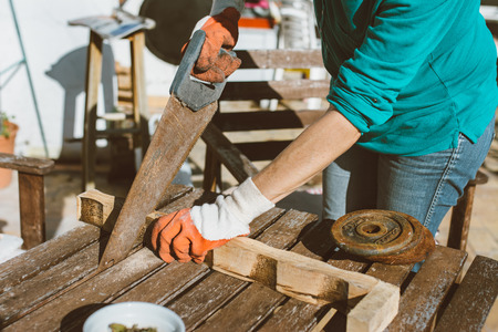 Woman sawing a wood, with work gloves on the table in the terrace of home. of day, outdoorの写真素材