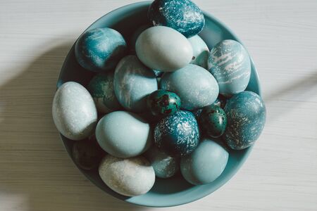 Naturally dyed Easter blue eggs, scattered on blue plate, on white wooden board. View from aboveの写真素材