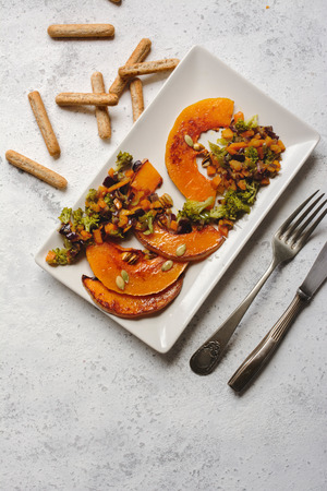 sliced baked pumpkin, with broccoli and assorted vegetables, on rectangular white plate, from aboveの写真素材