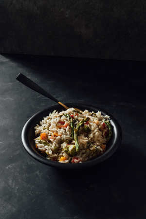 Bowl with basmati rice with sauteed vegetables, on black tableの写真素材