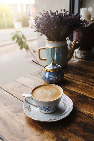 Cappuccino coffee, in vintage porcelain cup, on the wooden table with unfocused street view.の写真素材