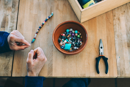 Woman making craft jewelry, with colored stones on wooden tableの写真素材