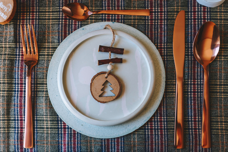 Holiday copper place setting, funny Christmas table dishes decorated with wooden ornaments and natural pine branches, on well plaid tablecloth, from aboveの写真素材