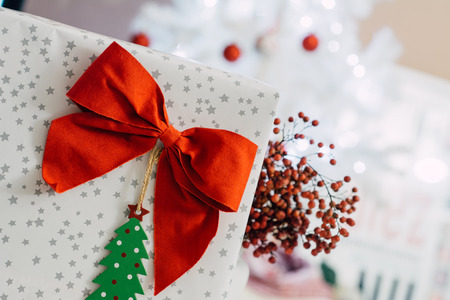 Gift with red bow and card, in front of white christmas tree, decorated with red balls.の写真素材