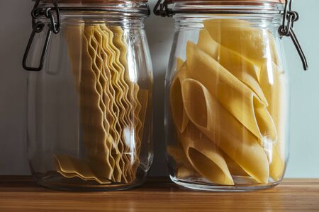 Glass jars with raw pasta, on the kitchen shelf, in front of the blue wallの写真素材