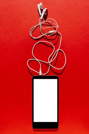 Mobile phone with blank screen and headphone on red  background. Top view with copy spaceの写真素材