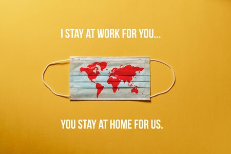Surgical mask with a red map of the world, with message "STAY AT HOME " Concept of global spread of Coronavirus Novel Covid-19. Coronavirus outbreak virus quarantine, yellow  background, nobodyの写真素材