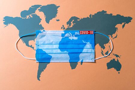 Surgical mask with a blue map of the world on the pink background, Concept of global spread of Covid-19. Coronavirus outbreak virus quarantine background,  concept of quarantine at home as preventative measure against coronavirus outbreak..の写真素材