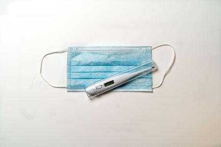 Surgical mask and digital thermometer on white background. Typical 3-ply surgical mask to cover the mouth and nose. Healthcare and medical conceの写真素材