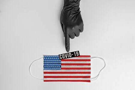 Doctors hand in black protective glove, points out surgical mask with the usa flag showing the message "covid-19"., Virus prevention and quarantine conceptの写真素材