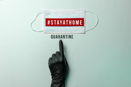 COVID-19, #STAYATHOME. Hand in black protective glove, points out surgical mask with showing the messageの写真素材