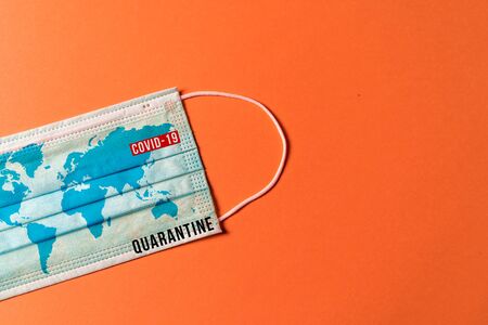 Surgical mask with a map of the world on orange background, Concept of global spread of Covid-19. Coronavirus outbreak virus quarantine background,  concept of quarantine at home as preventative measure against coronavirus outbreak..の写真素材