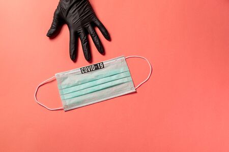 Covid-19. Doctor hand in black protective glove, points out surgical mask with copy space on pink background. Virus prevention and coronavirus quarantine concept on pink background.の写真素材