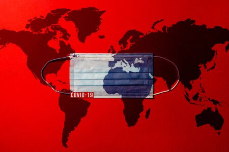 Surgical mask with a blue map of the world, on red background, Concept of global spread of Covid-19. Coronavirus outbreak virus quarantine background,  concept of quarantine at home as preventative measure against coronavirus outbreak..の写真素材