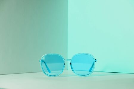 Modern blue sunglasses in front of the corner of the pastel wall background with copy space. Product photograph of minimalist concept with room for text, front viewの写真素材