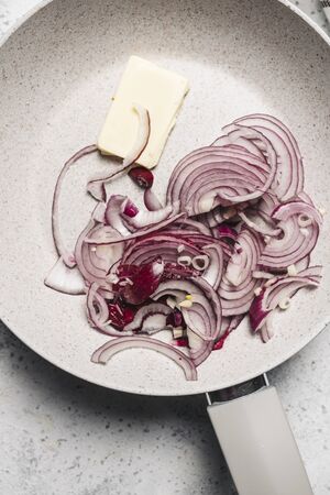 skillet with chopped red onion and butter on the kitchen fireの写真素材