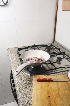 white skillet with cut red onion and butter, on the kitchen fire. Cooking in confinementの写真素材